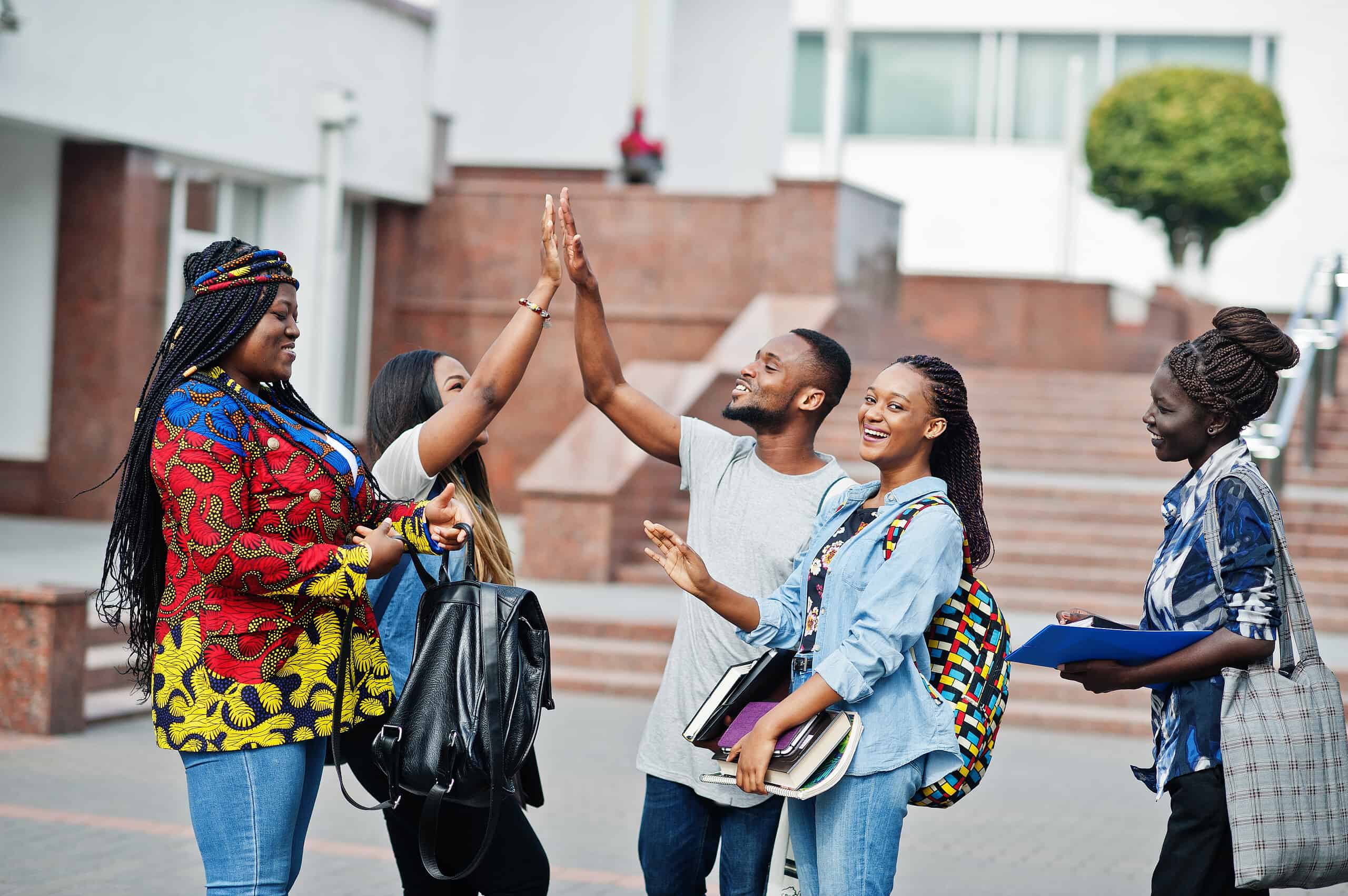 Group of five african college students spending time together on campus at university yard. Black afro friends studying and gives high five each other.
